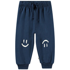 Simeon Pants by Molo. Navy joggers with elastic and drawstrings at the waist, smiley faces printed in white on the knees