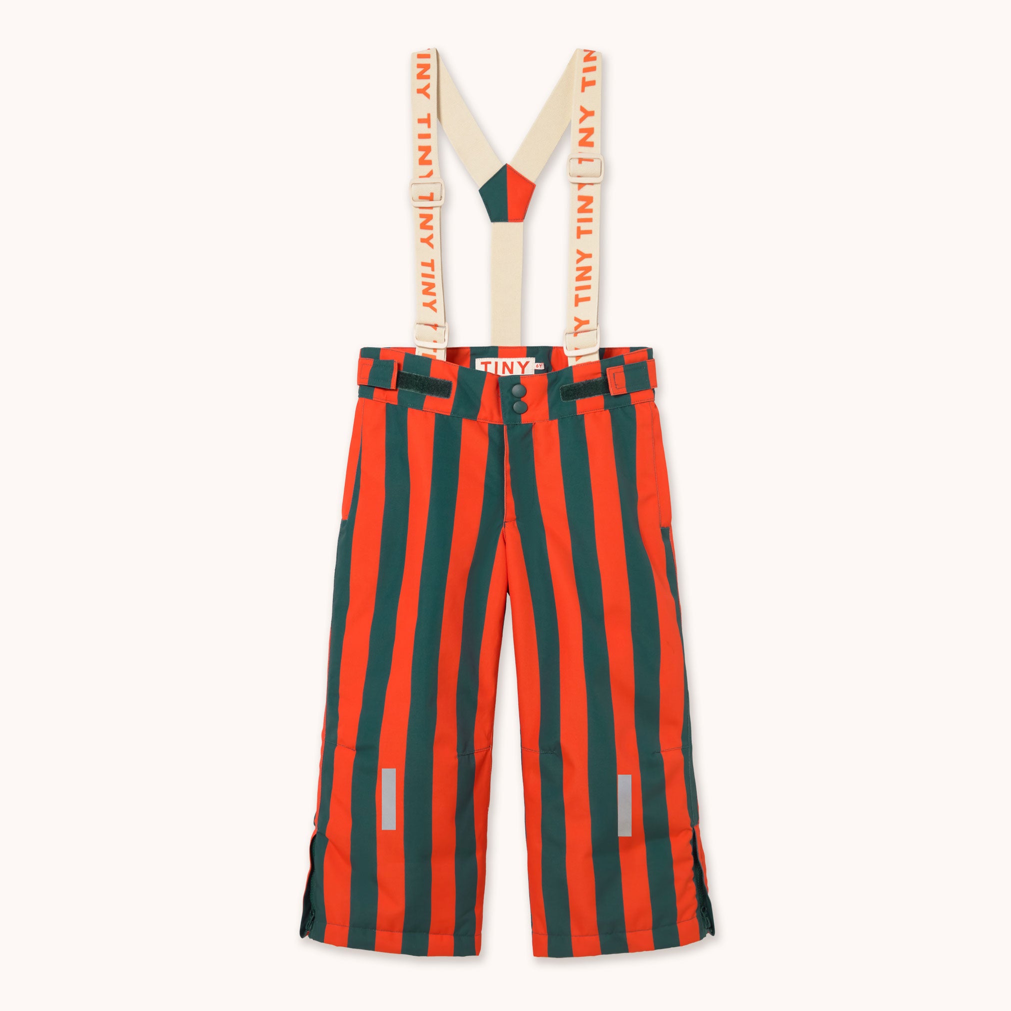A pair of striped snow pants with attached suspenders by designer Tiny Cottons, featuring bold vertical stripes in orange and dark green, with beige suspenders printed with 'TINY TINY TINY' in orange. The brand 'TINY' is also visible on the waistband label.