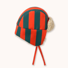 A red and dark green striped winter chapka hat by designer Tiny Cottons with cream-colored faux fur ear flaps and red chin ties, shown on a light cream background.