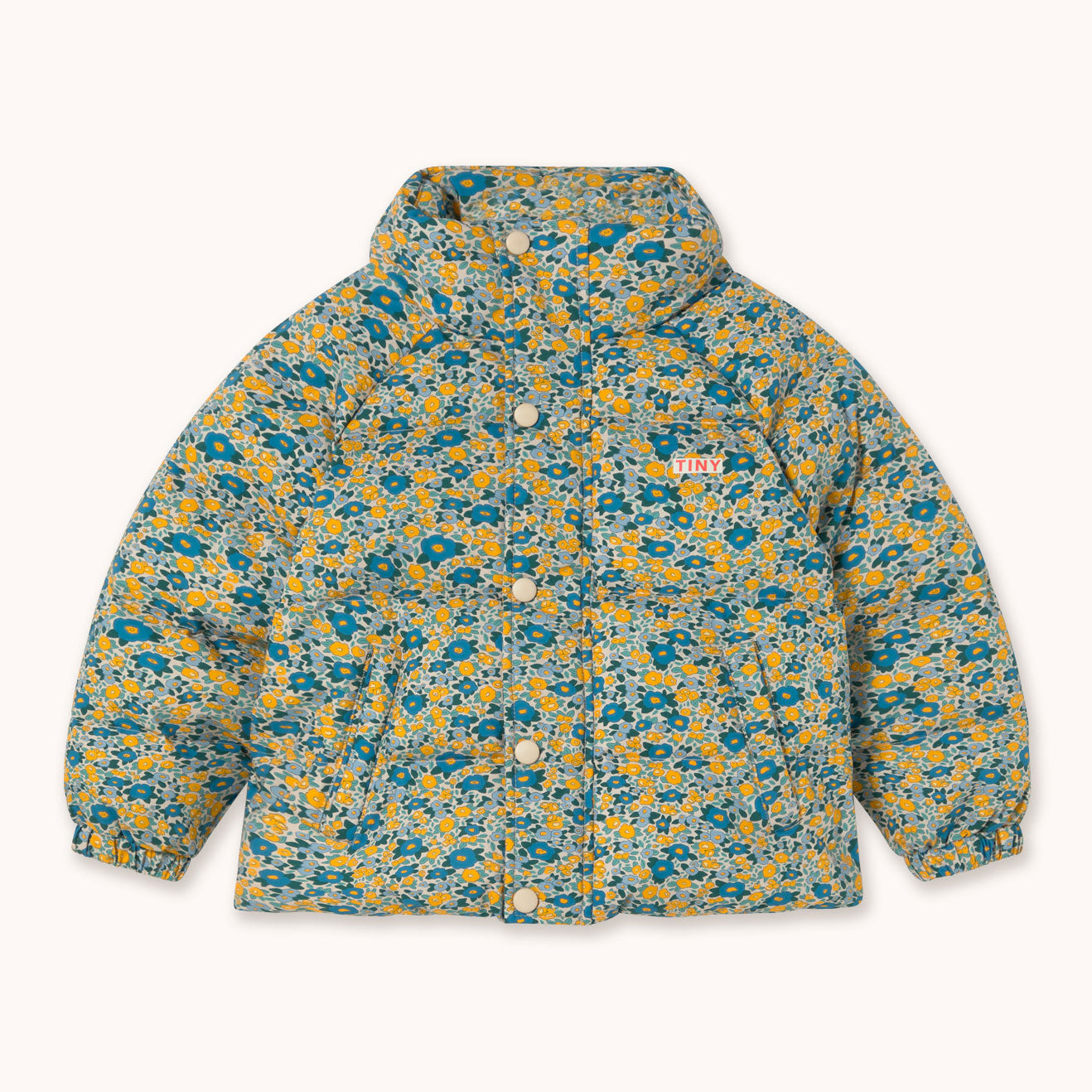 A hooded puffer jacket by designer Tiny Cottons with a dense abstract floral pattern in teal, yellow, and off-white, featuring a button-up front and a small 'TINY' logo on the chest.