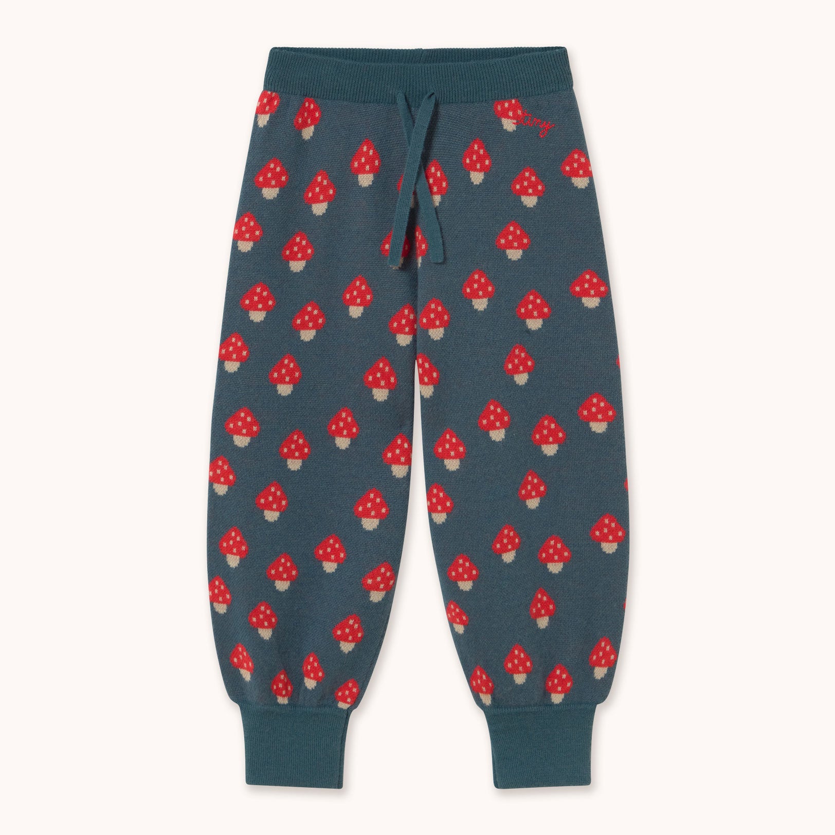 A pair of dark teal sweatpants by designer Tiny Cottons with an all-over red and white mushroom print, featuring a matching dark teal drawstring waist and ribbed cuffs.