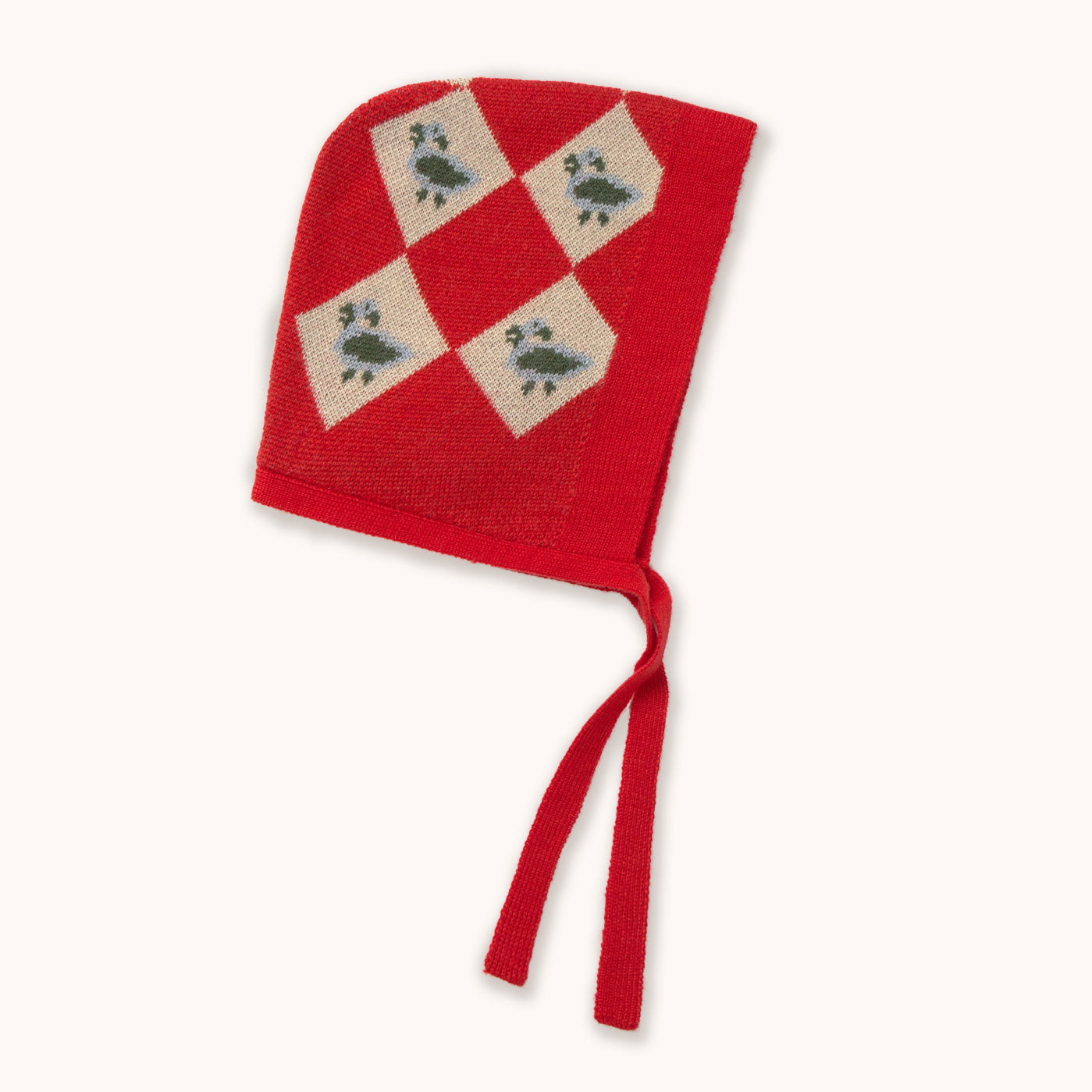 A red knit bonnet by designer Tiny Cottons with cream diamond panels featuring green birds, tied with red strings, shown on a plain off-white background.