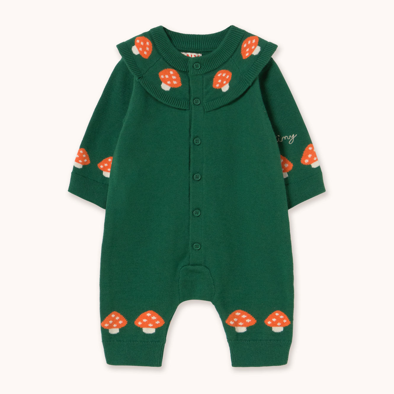 A dark green long-sleeve baby romper by designer Tiny Cottons with a button-up front, a wide ribbed Peter Pan collar decorated with orange and white mushrooms, and matching mushroom prints on the cuffs and ankles.