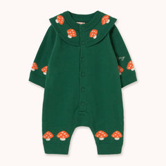 A dark green long-sleeve baby romper by designer Tiny Cottons with a button-up front, a wide ribbed Peter Pan collar decorated with orange and white mushrooms, and matching mushroom prints on the cuffs and ankles.