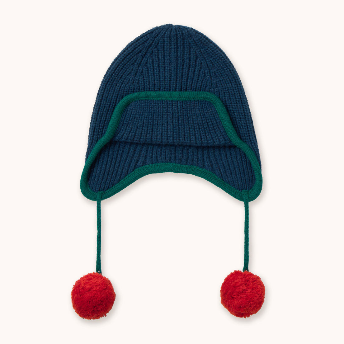 A navy blue ribbed knit winter hat by designer Tiny Cottons with ear flaps, a dark green trim, and two red pom-poms hanging from the sides, shown against a plain off-white background.