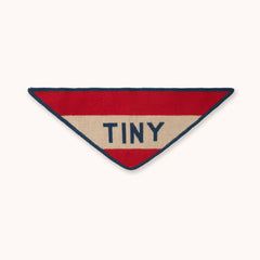 A bandana by designer Tiny Cottons - a triangular patch with horizontal red and beige stripes, outlined in navy blue, with the word 'TINY' in navy text across the center, shown on a plain off-white background.