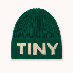 A dark green ribbed knit beanie hat by designer Tiny Cottons with the word 'TINY' knitted in cream-colored letters across the folded cuff, shown against a plain off-white background.