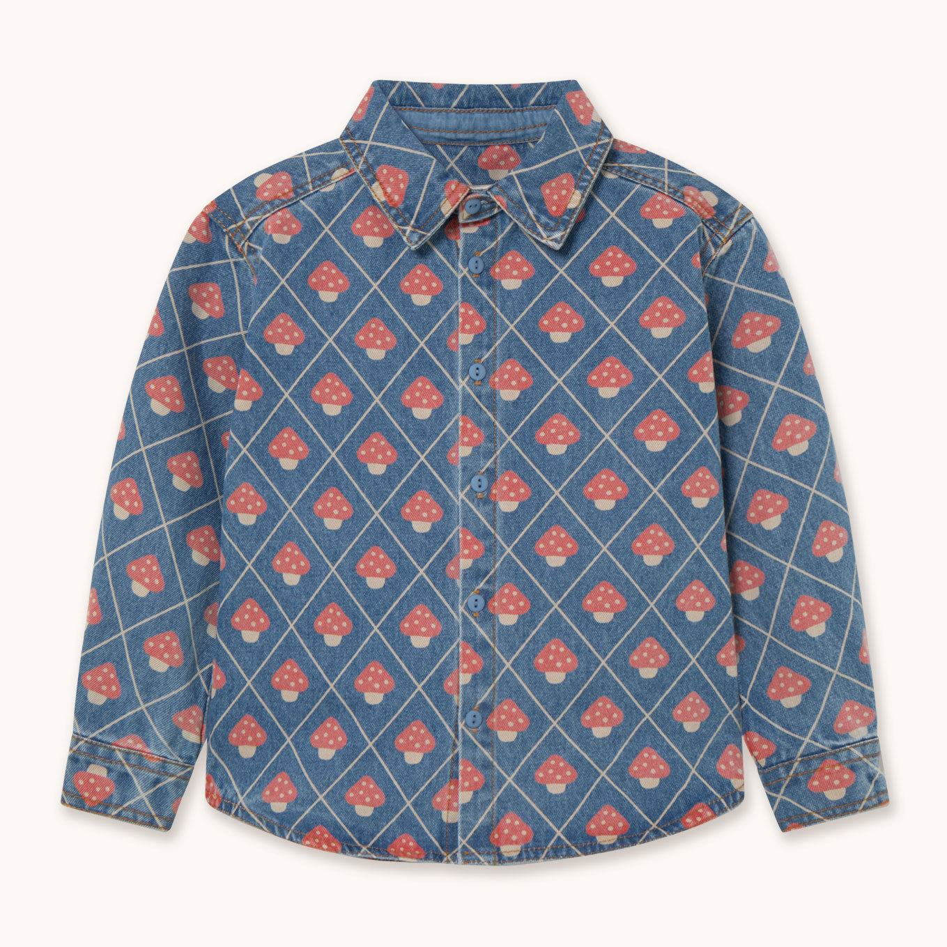 A long-sleeve button-up shirt by designer Tiny Cottons in blue denim featuring a repeating pattern of red and white mushrooms inside a diamond grid design, shown flat against a light cream background.