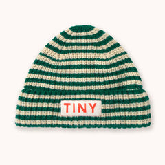 A green and cream striped knit beanie hat by designer Tiny Cottons with a white rectangular patch on the front cuff featuring the word 'TINY' in orange-red letters, shown against a plain off-white background. 