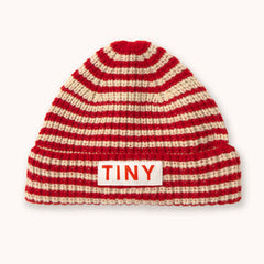 A red and cream striped knit beanie hat by designer Tiny Cottons with a white rectangular patch on the front cuff featuring the word 'TINY' in red.