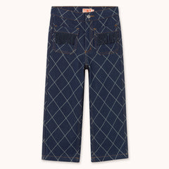 A pair of dark blue denim pants featuring a white argyle pattern and fringed pocket details by designer Tiny Cottons, shown flat against a light cream background.