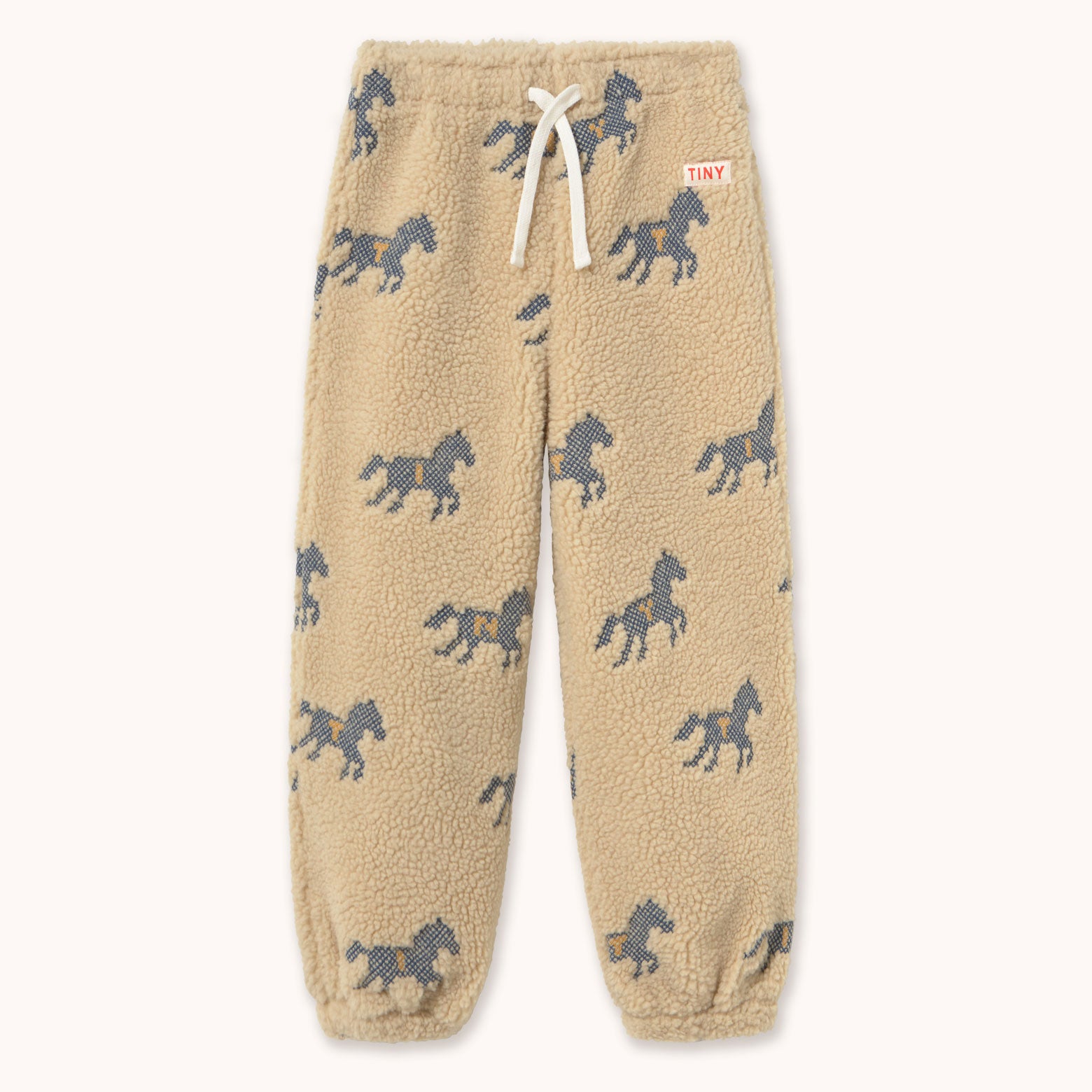 Beige sherpa fleece jogger pants by designer Tiny Cottons with an all over dark gray horse print, featuring a white drawstring and a small red 'TINY' brand tag on the side.