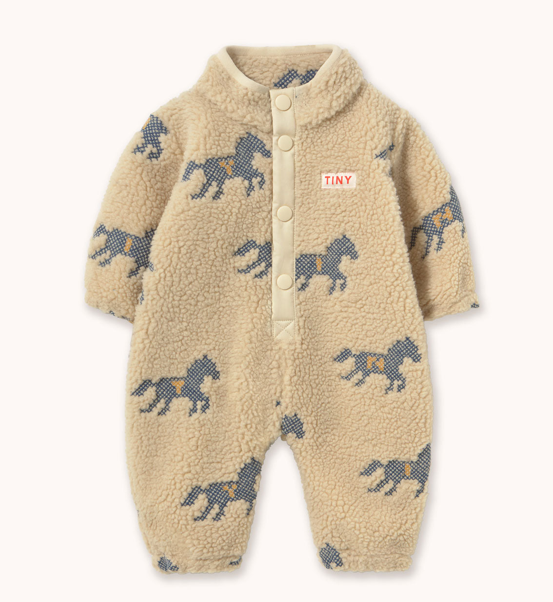 A baby's sherpa fleece one-piece romper in beige, by designer Tiny Cottons, featuring a pattern of dark blue horses with yellow accents and a small 'TINY' brand label on the chest. It has a button-up front and a mock neck collar.