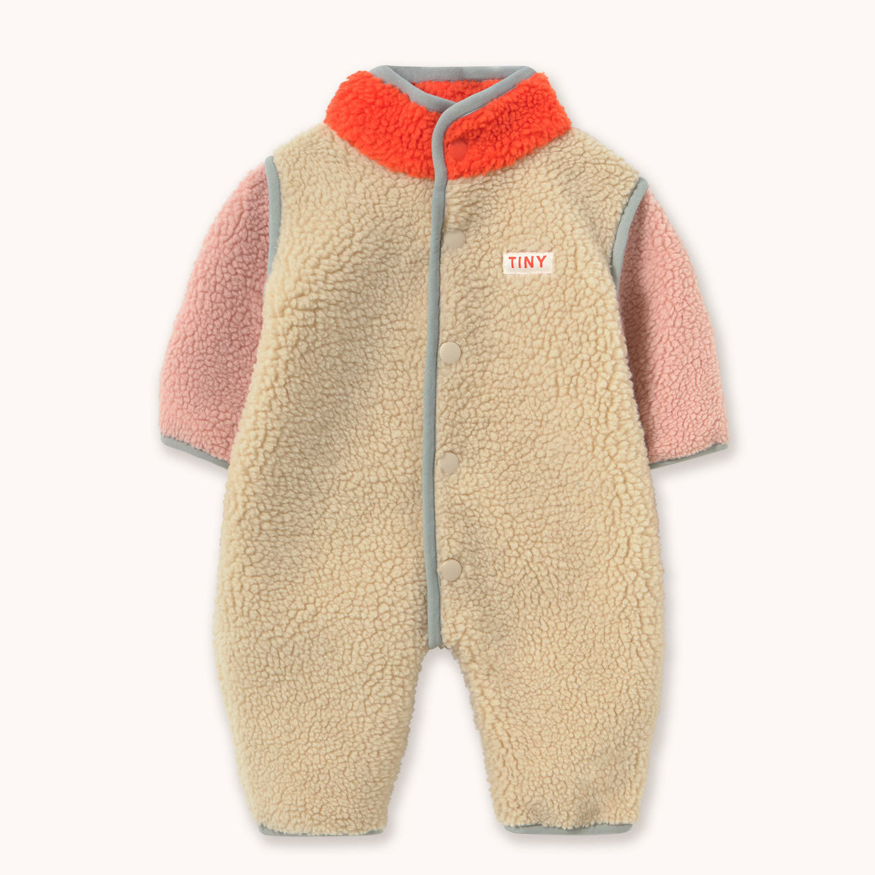 A baby fleece one-piece romper with a beige sherpa body, pink sleeves, a bright orange collar, and gray trim, featuring a small 'TINY' brand patch on the chest. By designer Tiny Cottons.