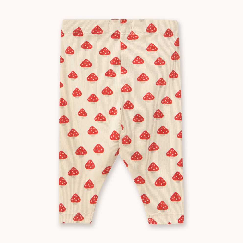A pair of cream-colored baby leggings  by designer Tiny Cottons, with a repeating red mushroom print, displayed flat against a light off-white background.