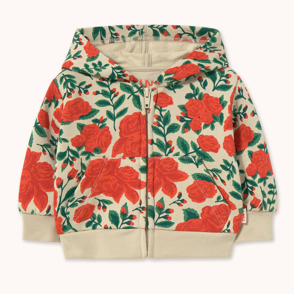 A children's zip-up hoodie by designer Tiny Cottons featuring a vibrant red rose and green leaf floral pattern on a warm beige background, with solid beige ribbed cuffs, hem, and hood lining.