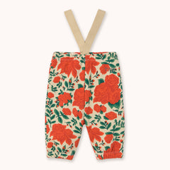 A pair of baby pants with beige suspenders by designer Tiny Cottons, featuring a vibrant red rose and green leaf floral pattern on a cream background.