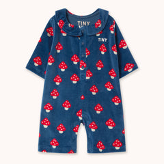 A baby romper by designer Tiny Cottons in navy blue velour with an all-over red and white mushroom print, featuring a Peter Pan collar, snap-button front, and 'TINY' branding on the chest.