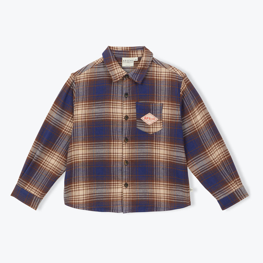 The Plaid Shirt from Arsene et Les Pipelettes is made from brown and blue plaid flannel fabric with pale brown faux fur lining. Featuring a shirt collar, long sleeves with ribbed cuffs, fully buttoned front opening, a patch pocket at the chest with the signature "AP &amp; Co" badge, and a small flag label inserted in the side seam.