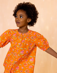 Child wearing an orange floral dress against a beige background