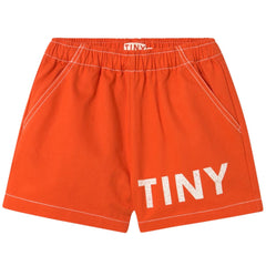 The Solid Logo Short from Tiny Cottons. Bright red shorts feature a relaxed straight fit, an elastic waistband, and pockets.